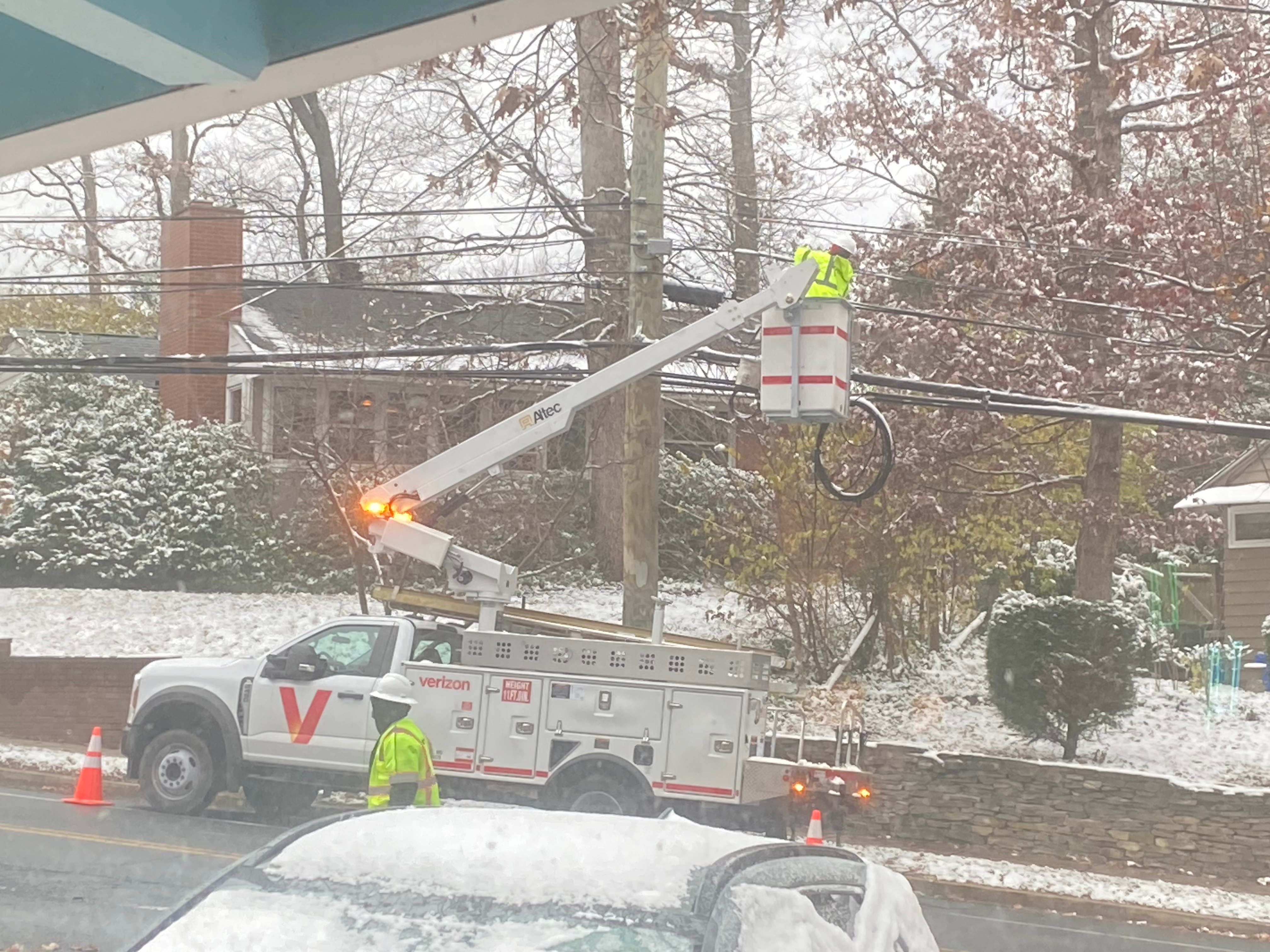 two Verizon workers repairing a cable, one of whom is up in a bucket truck against a pole